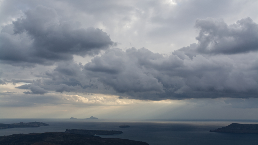 Dark clouds and a sunbeam above Santorini archipelago